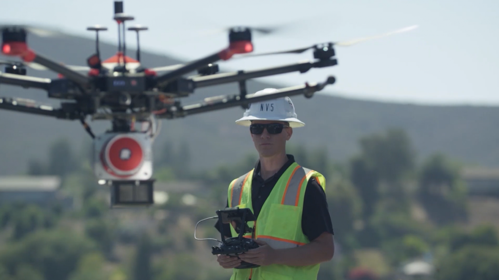 Man wearing white NV5 hard hat with safety vest piloting drone for aerial drone survey